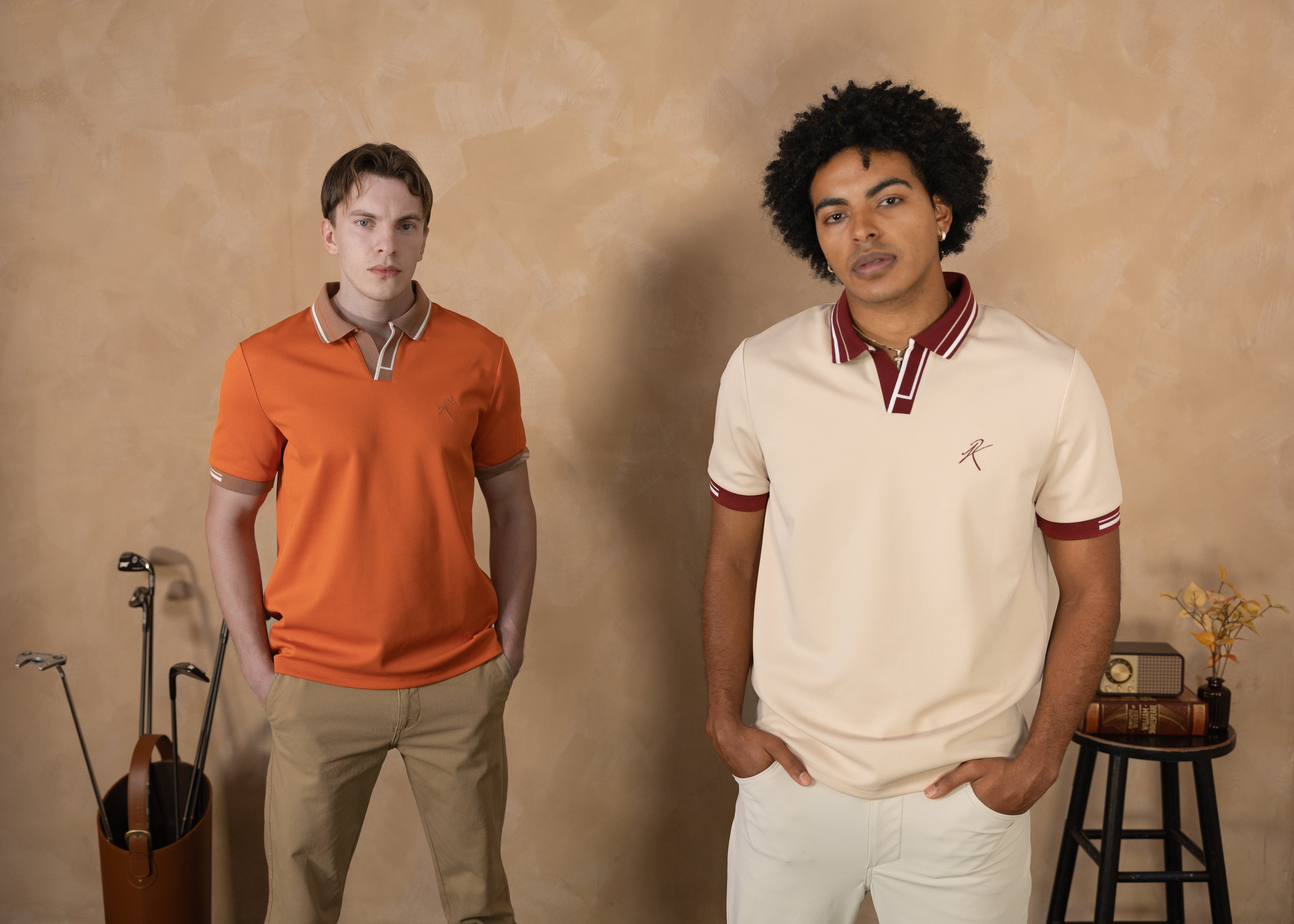 Two men wearing polo shirts standing against a beige wall.
